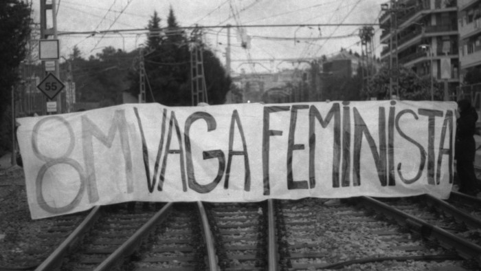 Manifestants subjectant una pancarta amb el lema "8M vaga feminista" a les vies del tren.